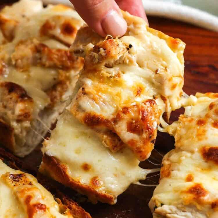 Hand picking up a cheesy slice of chicken Alfredo garlic bread with melted mozzarella and golden ciabatta.
