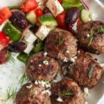 six Greek meatballs, Keftedes, in a bowl with tzatziki sauce and Greek salad.