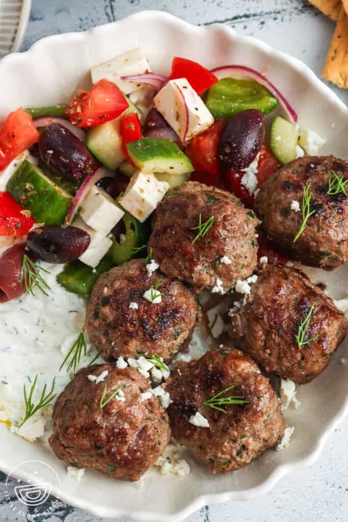 six Greek meatballs, Keftedes, in a bowl with tzatziki sauce and Greek salad.
