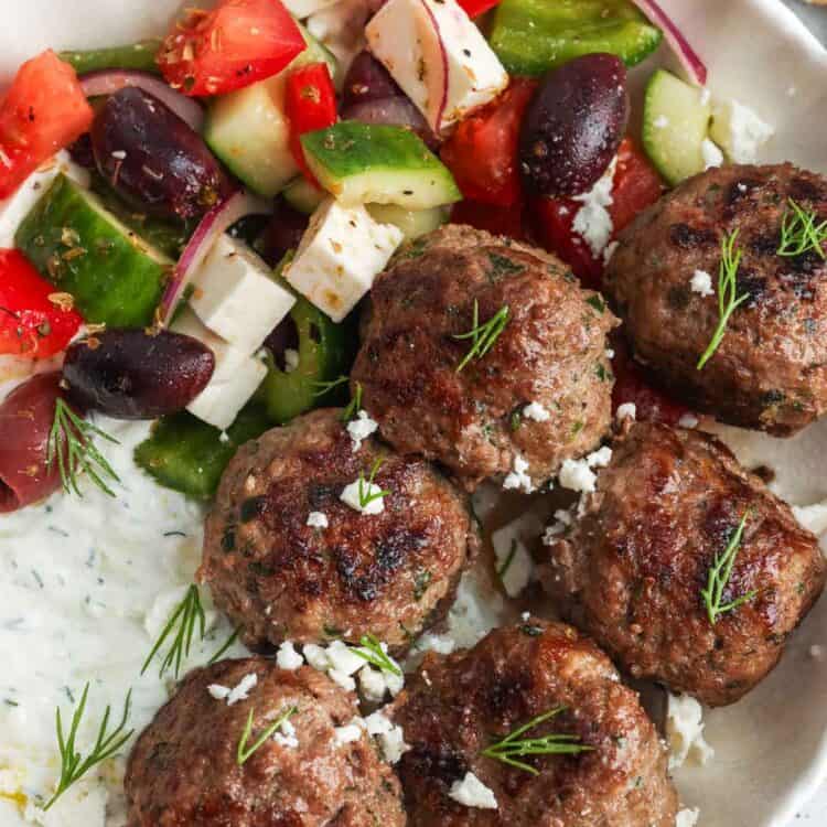 six Greek meatballs, Keftedes, in a bowl with tzatziki sauce and Greek salad.
