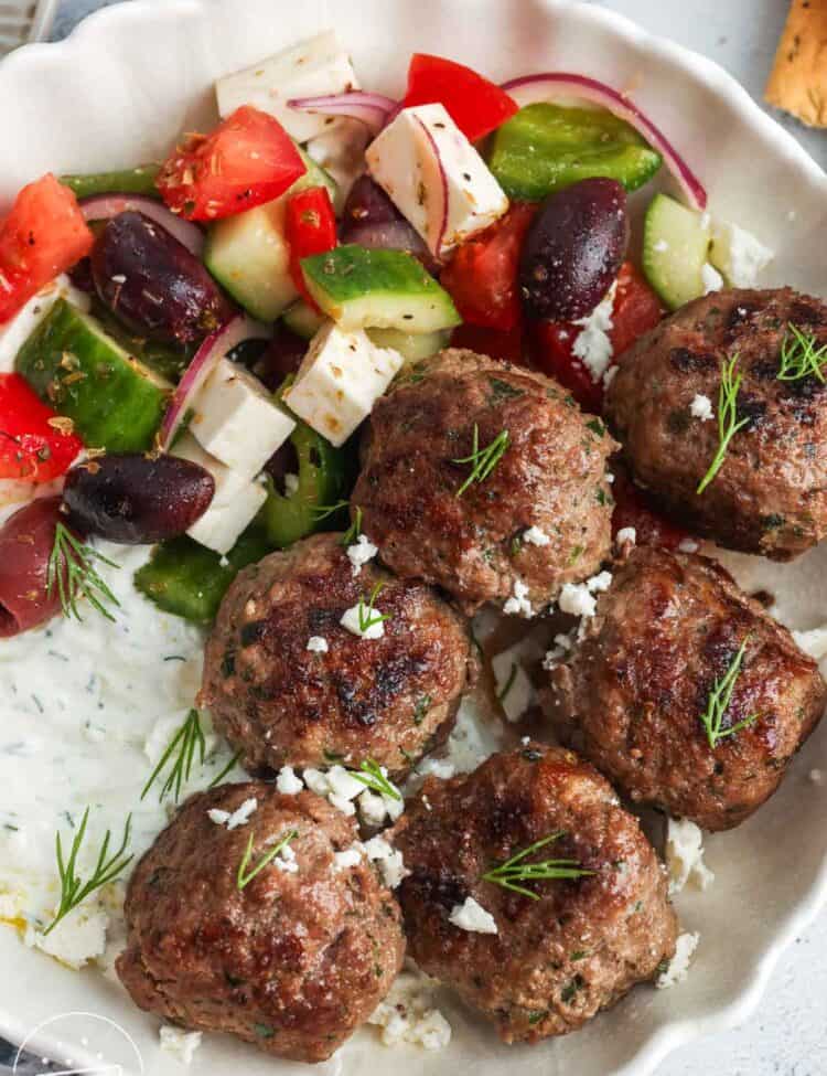 six Greek meatballs, Keftedes, in a bowl with tzatziki sauce and Greek salad.