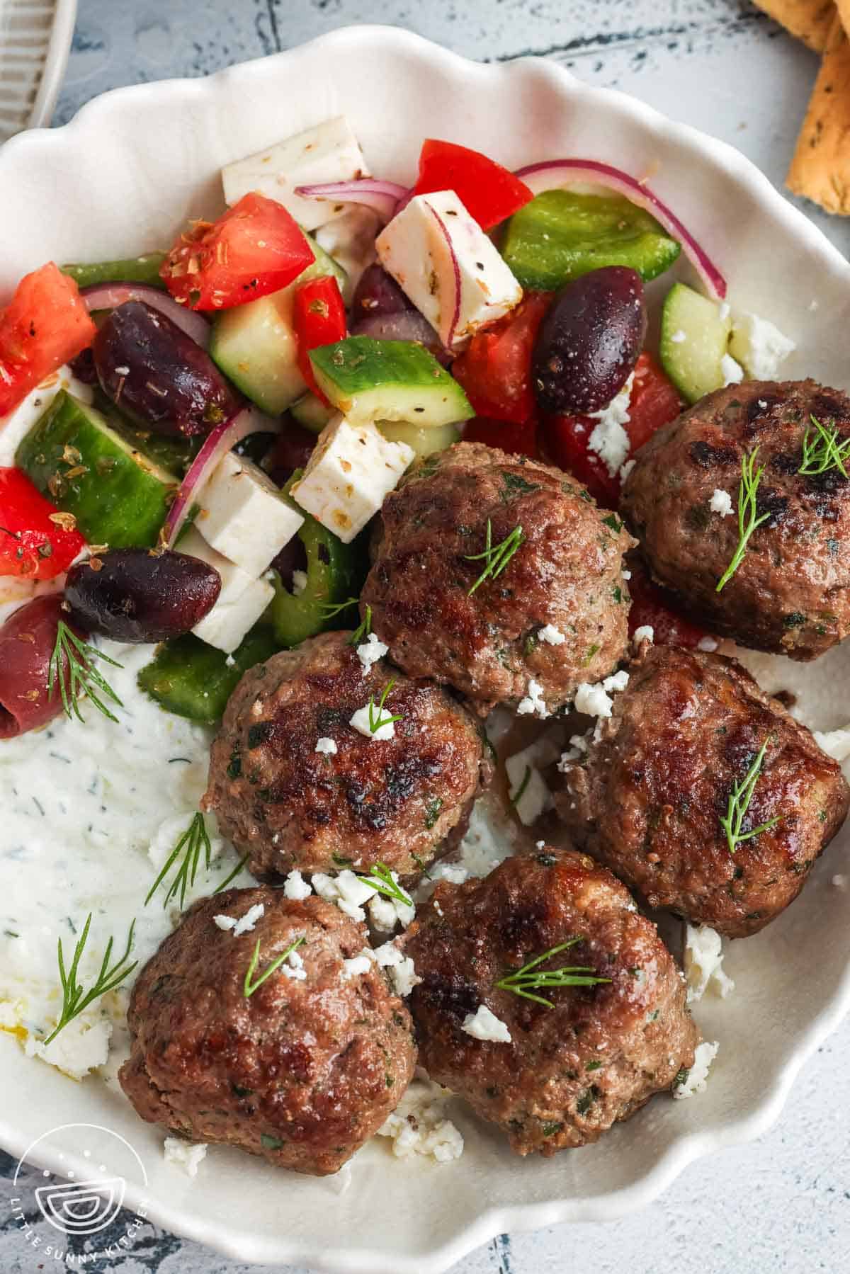 six Greek meatballs, Keftedes, in a bowl with tzatziki sauce and Greek salad.