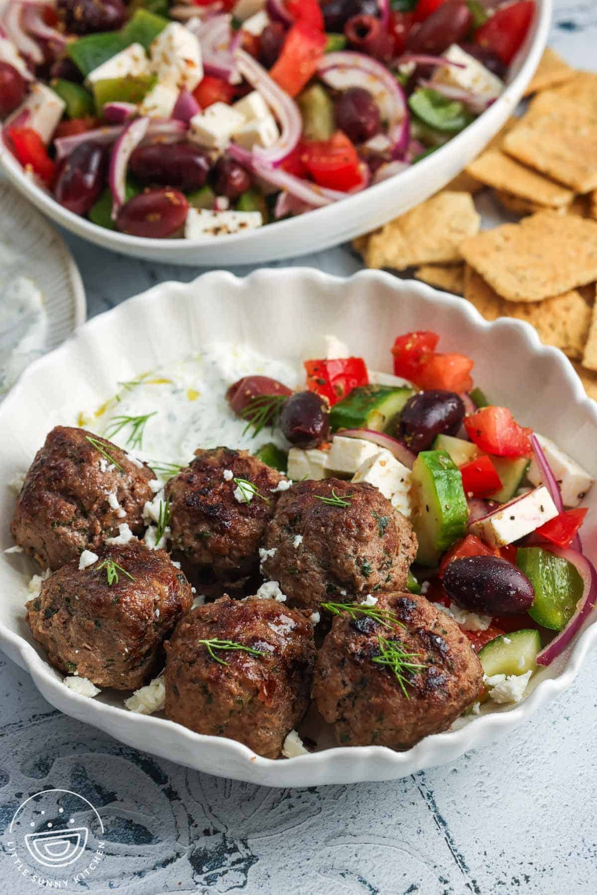 A serving of Greek style all beef meatballs with a side of tzatziki and greek salad.