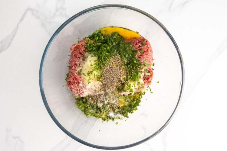 Ground beef, herbs, and seasonings in a glass mixing bowl.