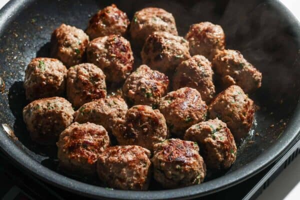 Greek meatballs cooked in a skillet until they're browned on all sides.