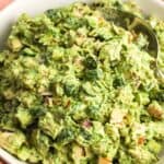 Green goddess chicken salad in a white bowl with diced cucumber, red onion, herbs, creamy avocado dressing, and sliced almonds.
