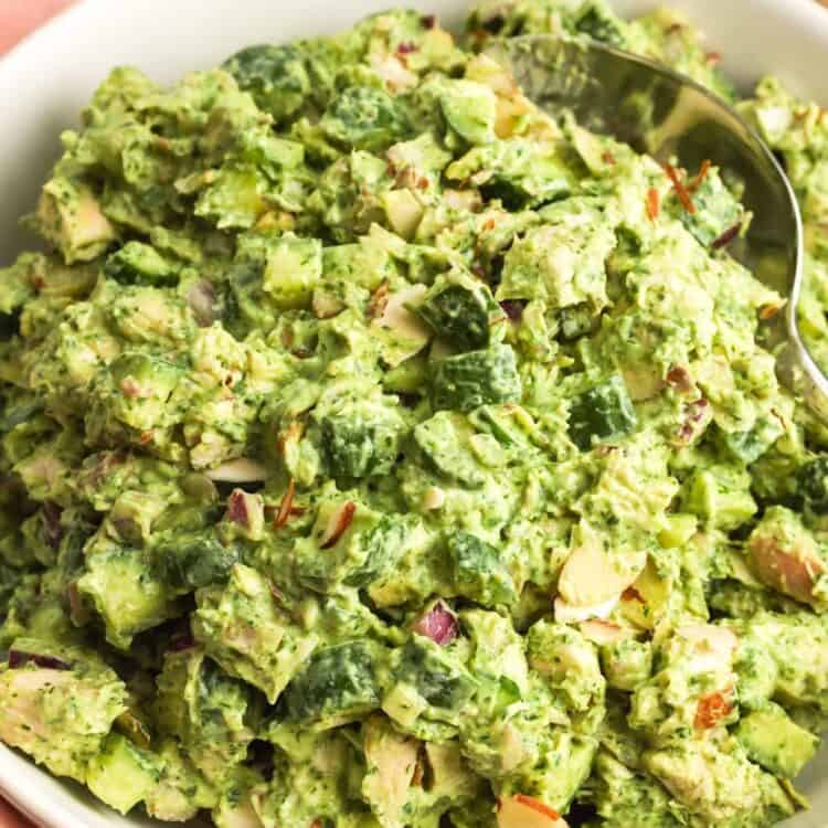 Green goddess chicken salad in a white bowl with diced cucumber, red onion, herbs, creamy avocado dressing, and sliced almonds.