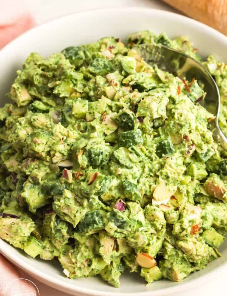 Green goddess chicken salad in a white bowl with diced cucumber, red onion, herbs, creamy avocado dressing, and sliced almonds.
