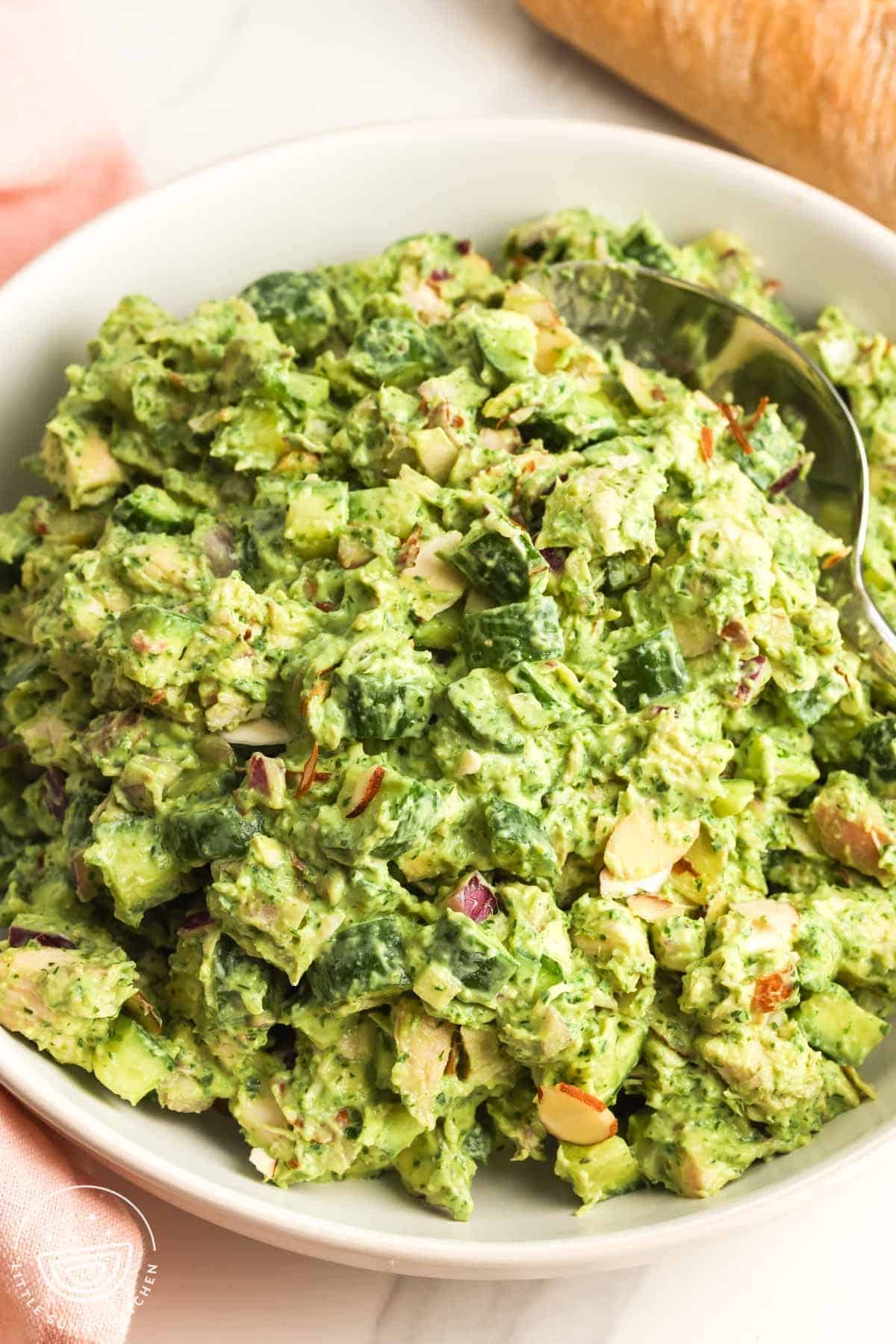 Green goddess chicken salad in a white bowl with diced cucumber, red onion, herbs, creamy avocado dressing, and sliced almonds.