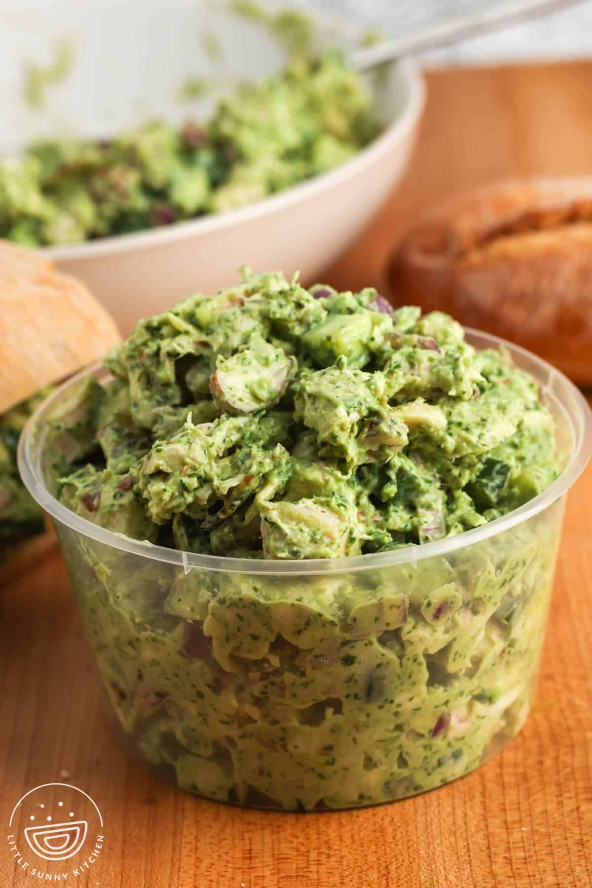 Creamy green goddess chicken salad packed in a container with bread in the background.