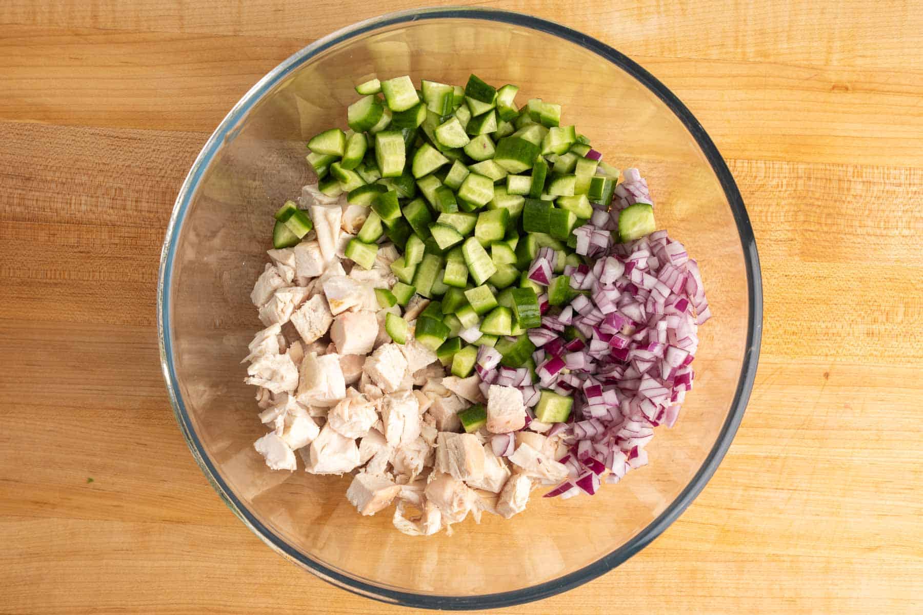 Chopped chicken, diced cucumber, red onion, and scallions in a glass mixing bowl.