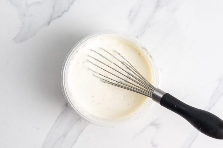 white sauce for halal cart bowls mixed in a deli container with a whisk.