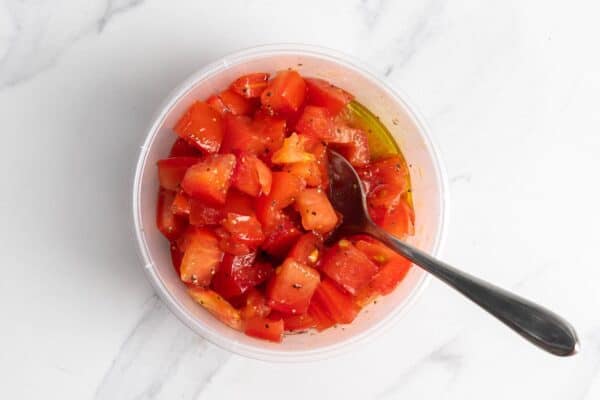 diced tomatoes in a deli container mixed with olive oil, salt, and pepper