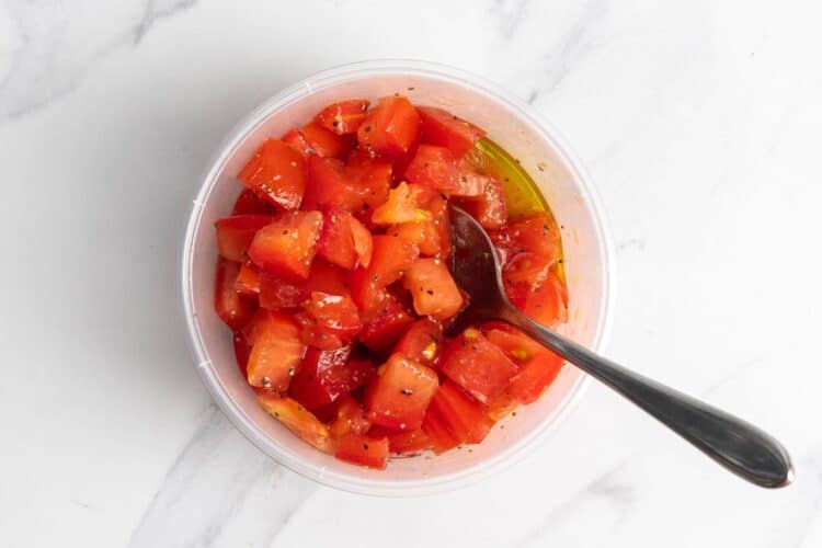 diced tomatoes in a deli container mixed with olive oil, salt, and pepper