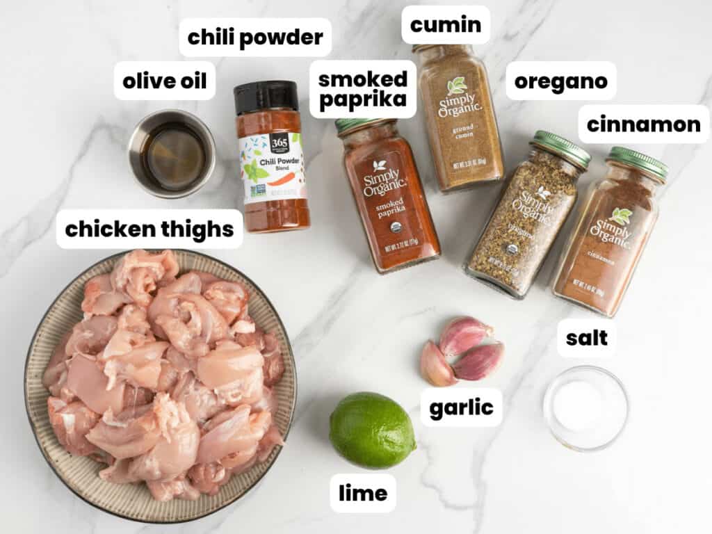 A bowl of chopped chicken thighs along with the seasonings needed to make street corn chicken bowls.