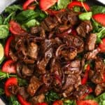 a plate of greens and tomatoes topped with Vietnamese shaking beef.