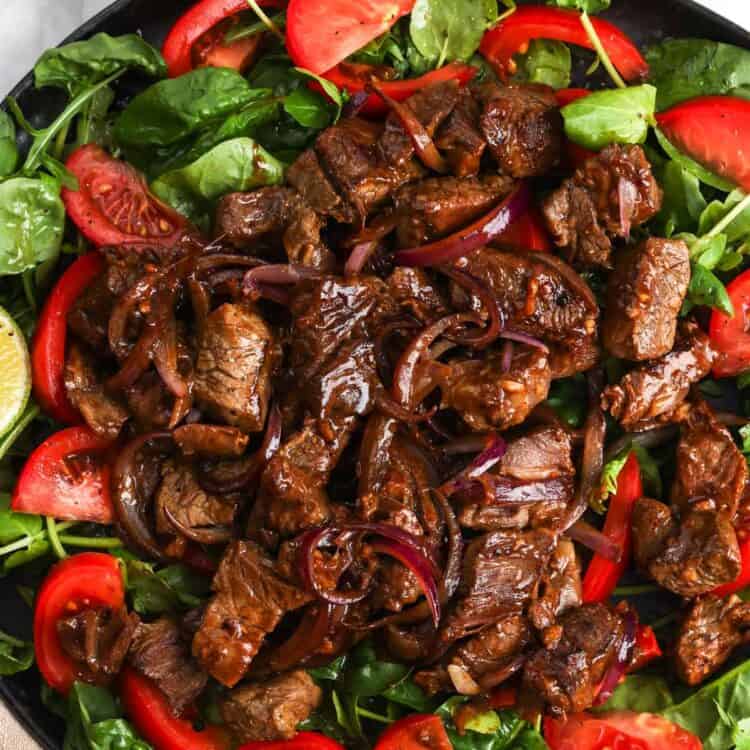 a plate of greens and tomatoes topped with Vietnamese shaking beef.