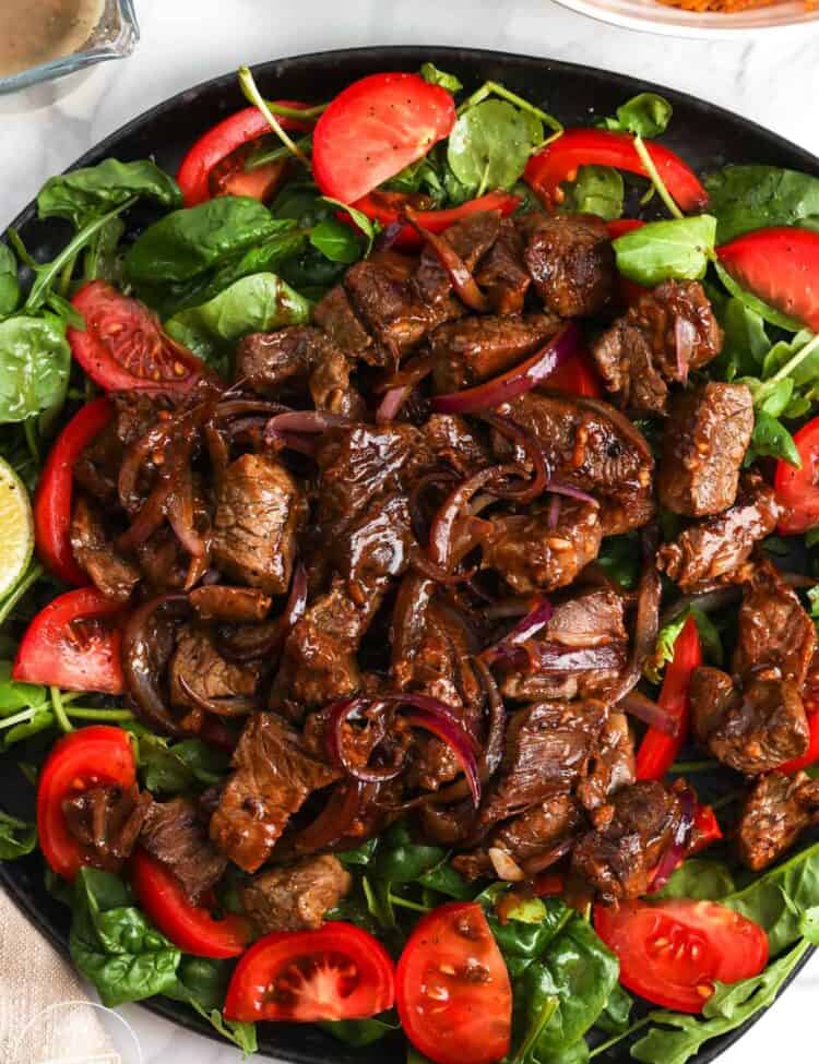 a plate of greens and tomatoes topped with Vietnamese shaking beef.