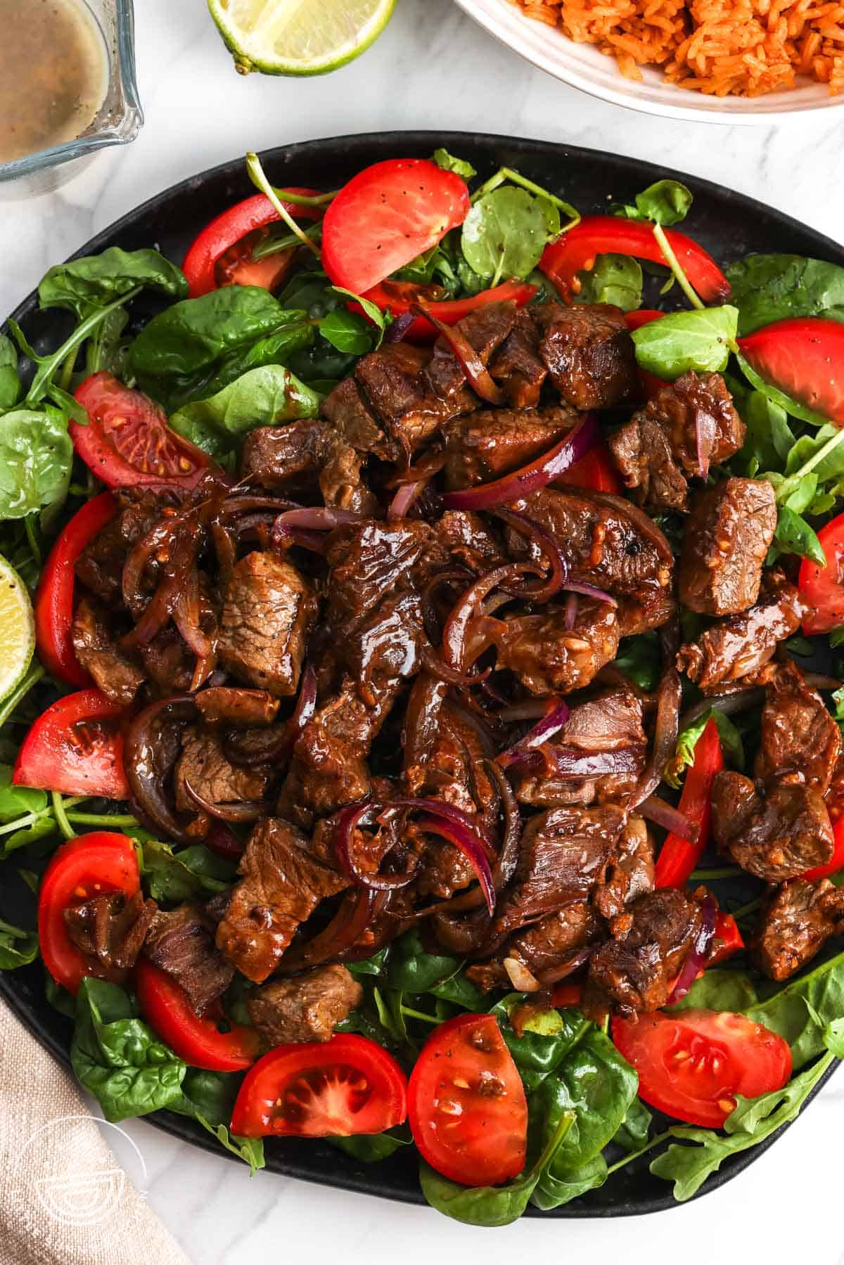 a plate of greens and tomatoes topped with Vietnamese shaking beef.