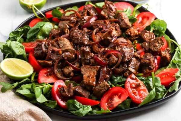 closeup of a platter of Vietnamese shaking beef served with salad and lime wedges.