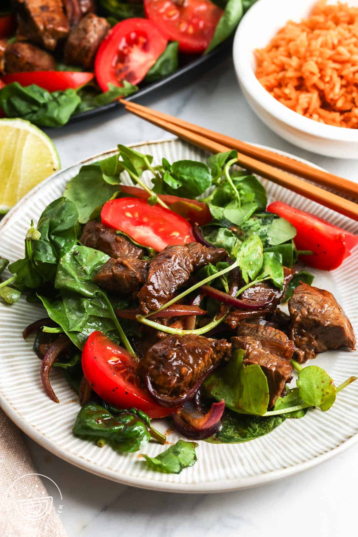 a serving on vietnamese shaking beef on a plate with chopsticks. Next to the plate is a bowl of rice.