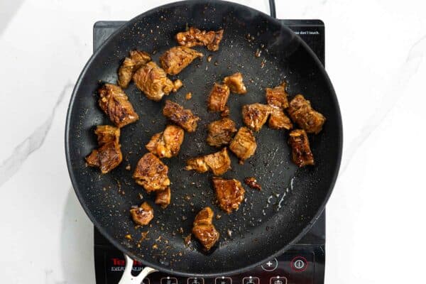 cubes of marinated beef cooking in a skillet.