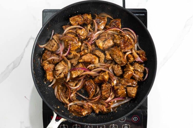 vietnamese shaking beef with onions cooking in a frying pan.