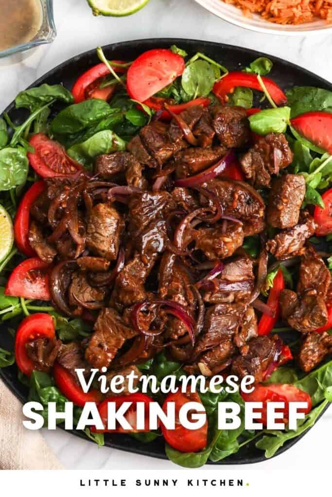 a plate of greens and tomatoes topped with Vietnamese shaking beef.