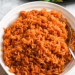 Bowl of fluffy Vietnamese tomato rice with a spoon and shaking beef with tomatoes in the background.