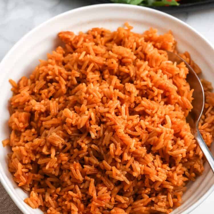 Bowl of fluffy Vietnamese tomato rice with a spoon and shaking beef with tomatoes in the background.