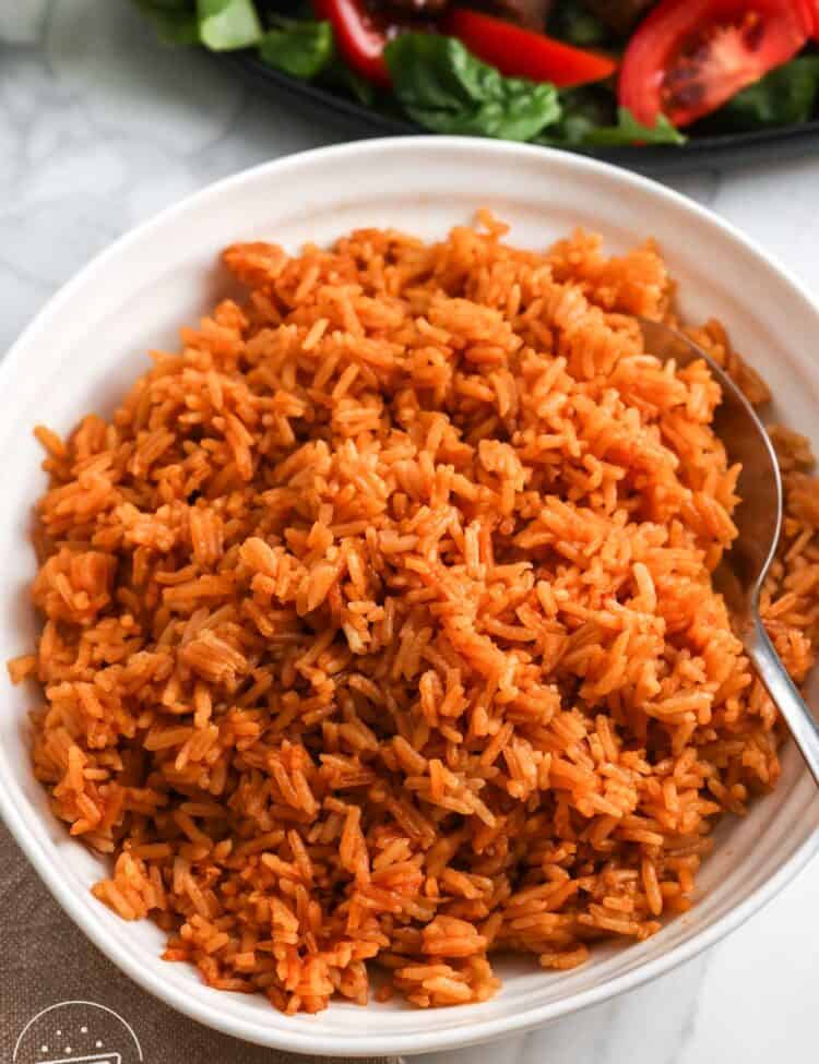 Bowl of fluffy Vietnamese tomato rice with a spoon and shaking beef with tomatoes in the background.