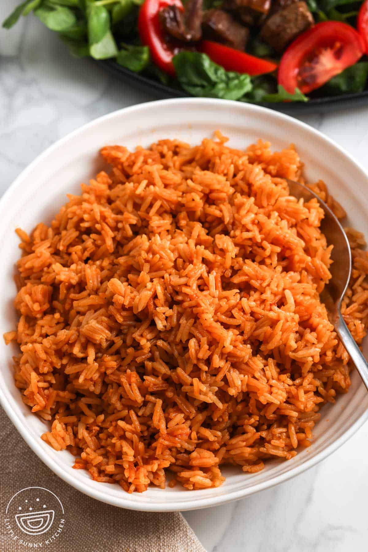 Bowl of fluffy Vietnamese tomato rice with a spoon and shaking beef with tomatoes in the background.