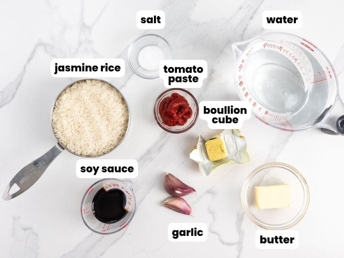Ingredients for Vietnamese tomato rice including jasmine rice, tomato paste, soy sauce, garlic, bouillon cube, butter, salt, and water.