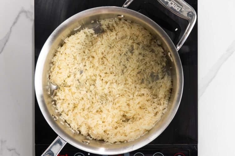 Rinsed jasmine rice being toasted in butter in a saucepan until the grains look glossy.