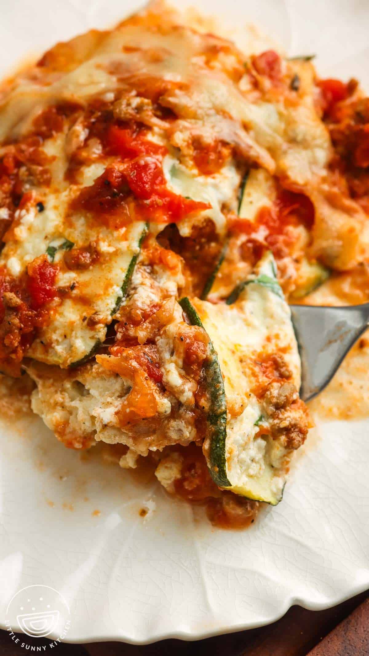 a serving of zucchini lasagna on a plate. A bite is on a fork.