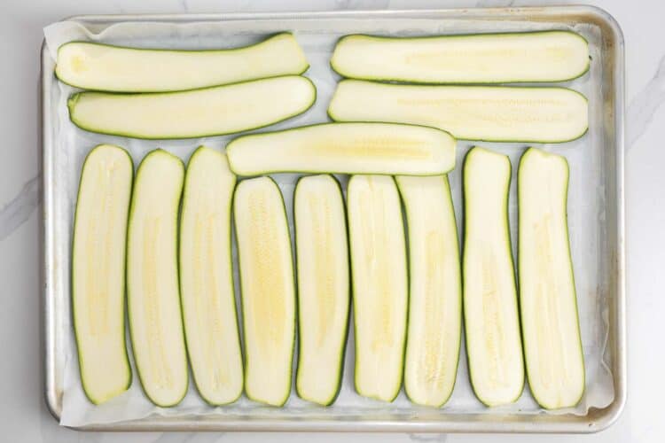 slices of zucchini arranged on a parchment lined baking sheet.
