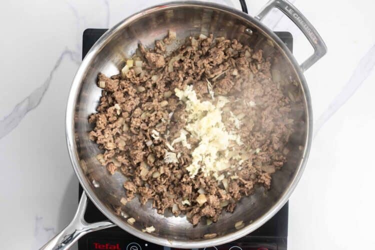 ground beef cooked with garlic and onions in a skillet.