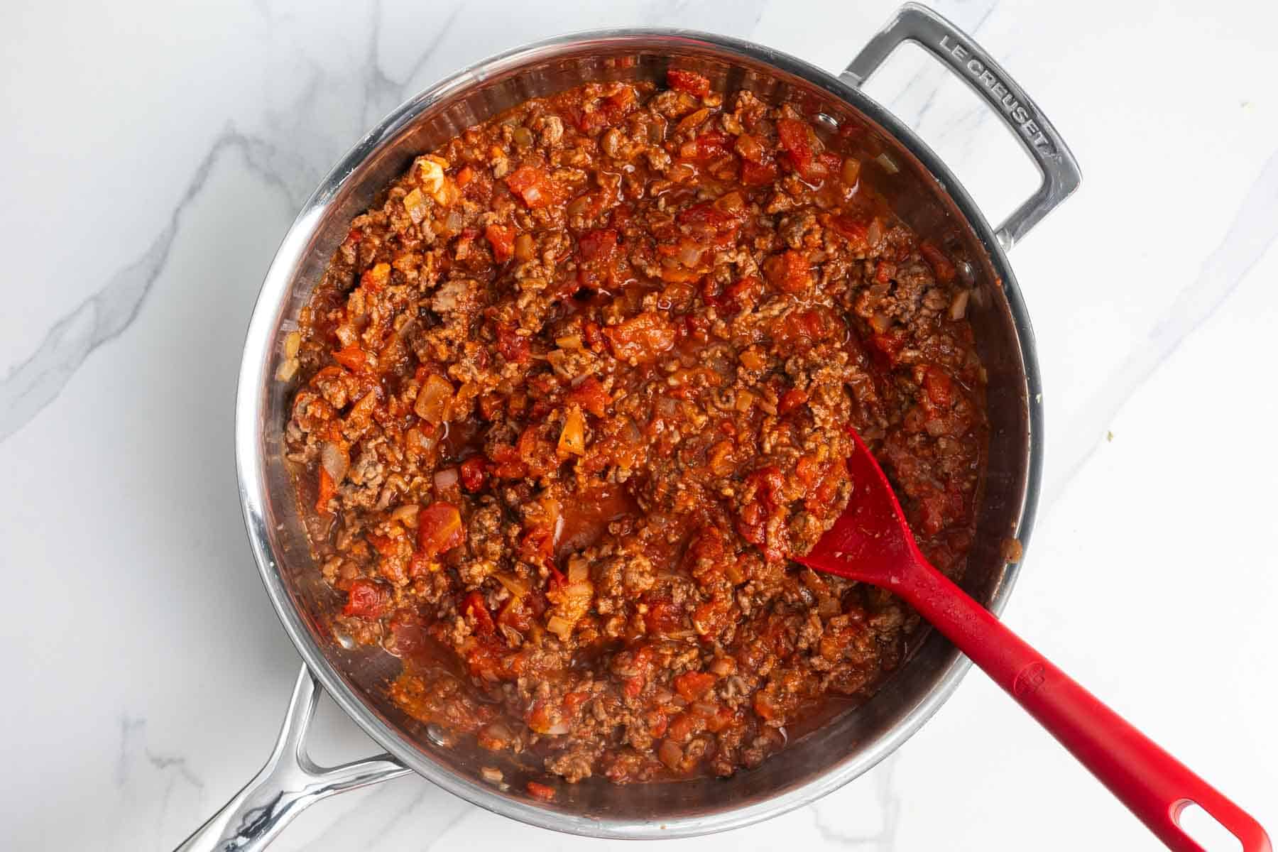 marinara added to cooked ground beef in a skillet.