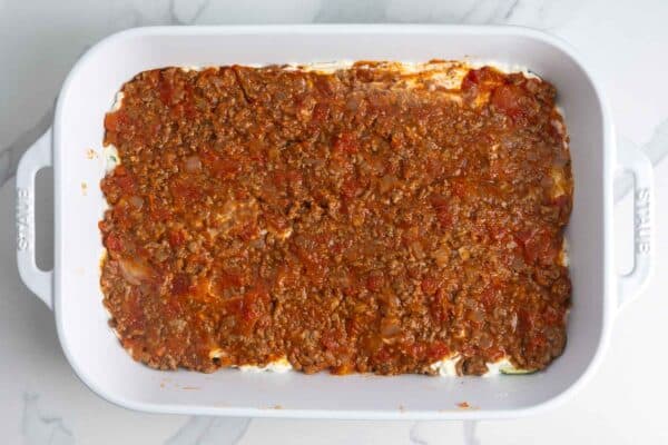 a layer of meat sauce over ricotta cheese and zucchini in a lasagna pan.