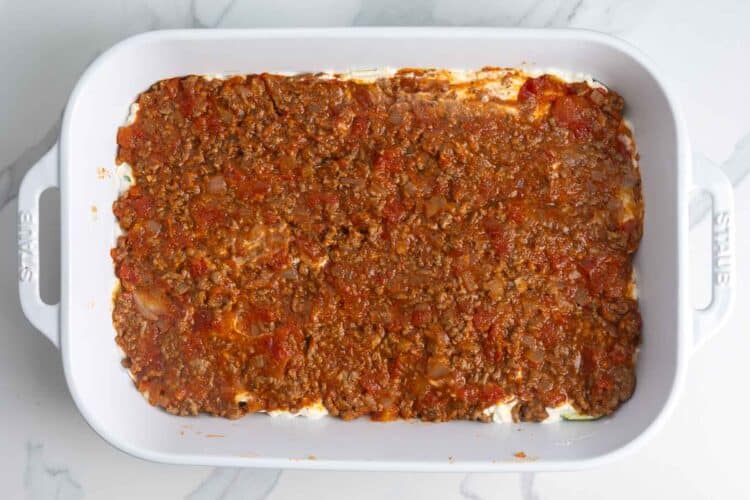 a layer of meat sauce over ricotta cheese and zucchini in a lasagna pan.