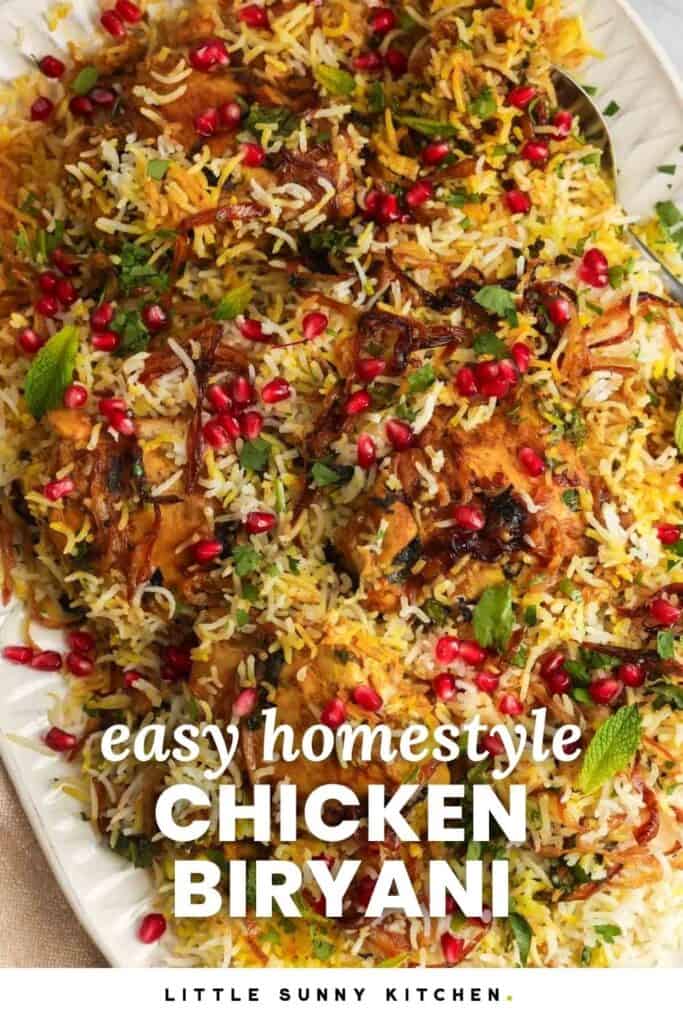 a platter of chicken biryani over saffron rice, topped with fried onions and pomegranate arils