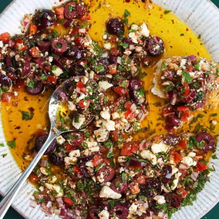 Mediterranean olive oil dip with olives, feta, tomatoes, herbs, and crusty bread in a shallow bowl.