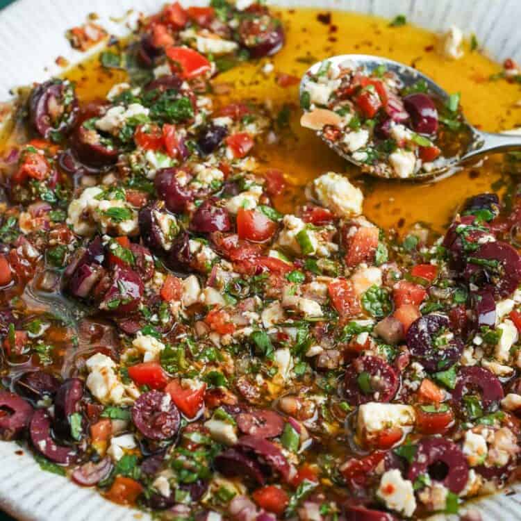 Mediterranean olive oil dip with olives, feta, tomatoes, herbs, and crusty bread in a shallow bowl.