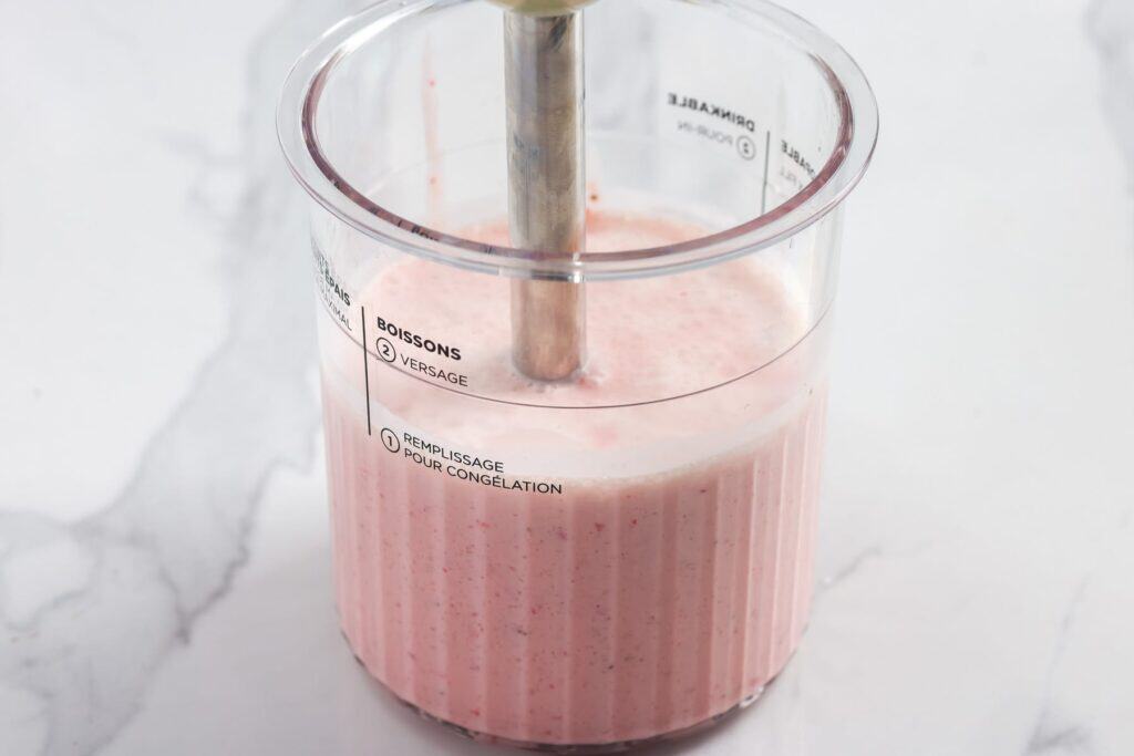Immersion blender blending strawberries and cream in a Ninja Creami pint