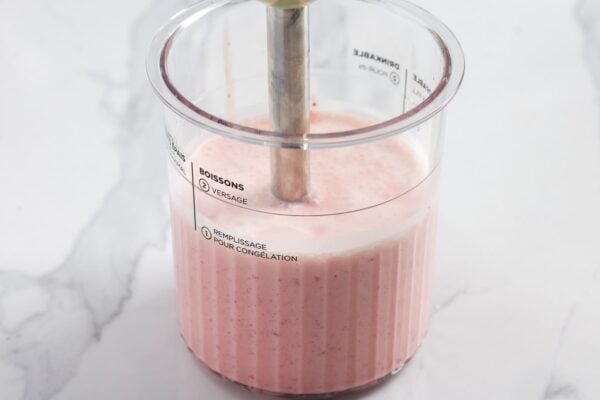 Immersion blender blending strawberries and cream in a Ninja Creami pint