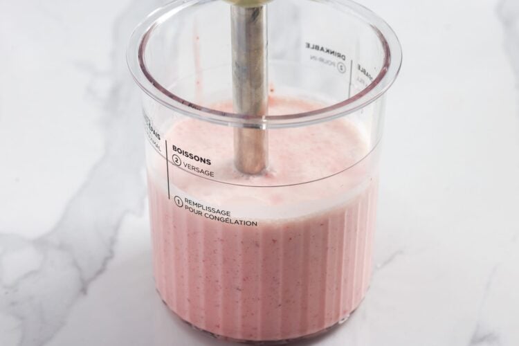 Immersion blender blending strawberries and cream in a Ninja Creami pint