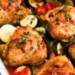 Close up of golden baked chicken thighs with zucchini, potatoes, tomatoes, and thyme.