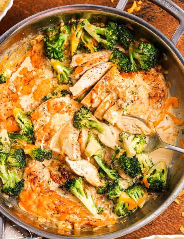 Creamy broccoli cheddar chicken in a skillet. next to the skillet are bowls of pasta.