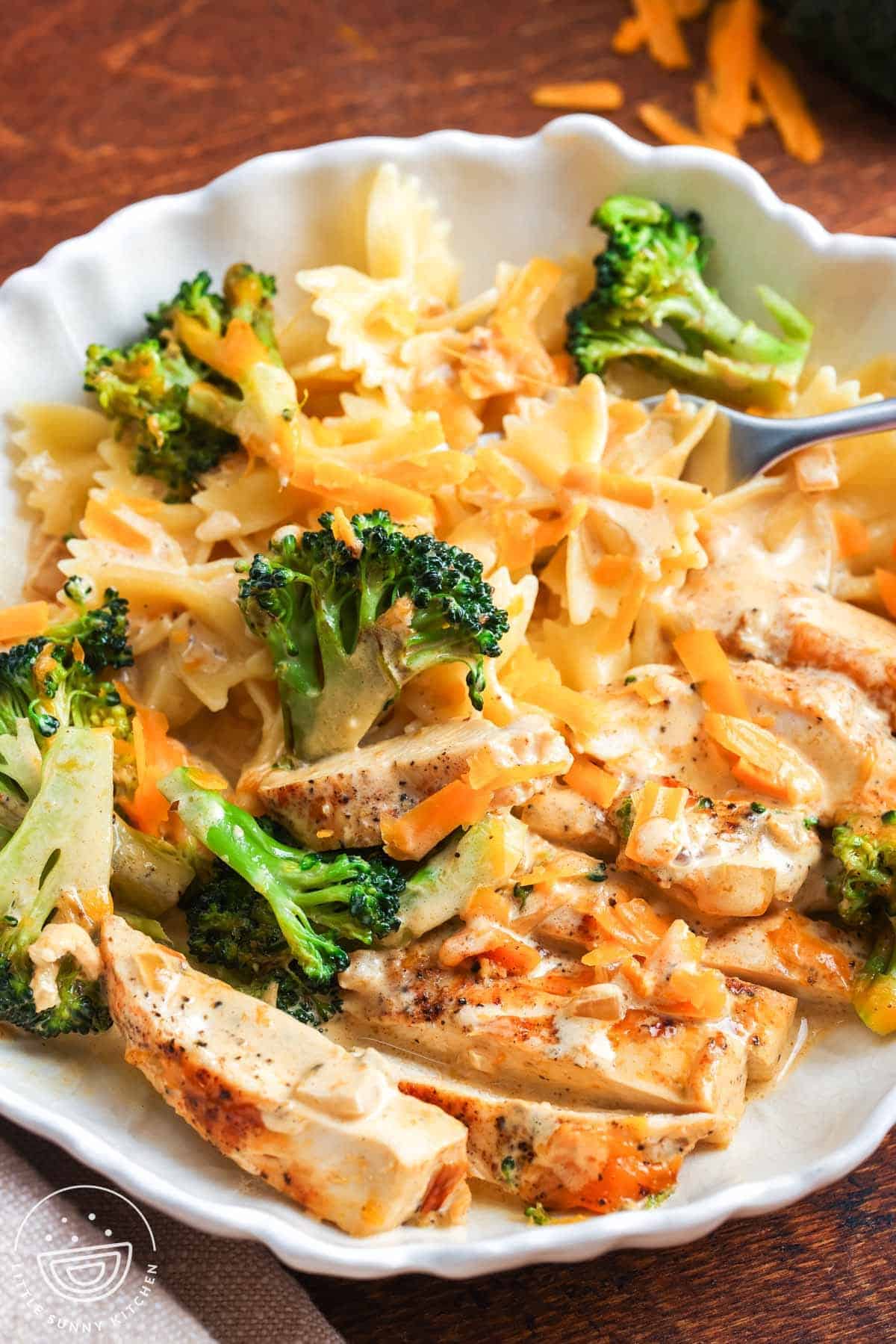 a bowl of pasta topped with sliced chicken and broccoli in a cheddar cheese sauce.