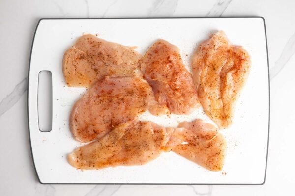 seasoned chicken cutlets on a white cutting board.